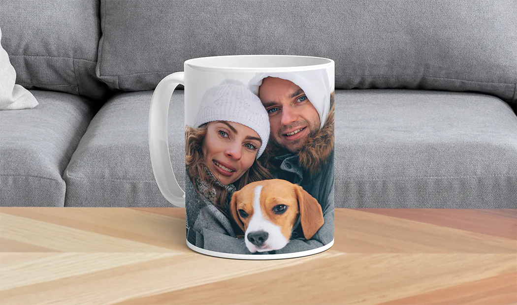 ["Personalised photo mugs from Printerpix", "Mother and baby holding a custom cartoon-design mug from Printerpix with 'Papa' text", "Personalised photo mug with a picture of a crawling baby in an animal onesie", "Mother and daughter holding custom-designed photo mugs with family photos", "Kissing couple with personalised mugs with text on them", "Personalised photo mug with your own photo of a dog on it", "", "", "", "", ""]||||||||||